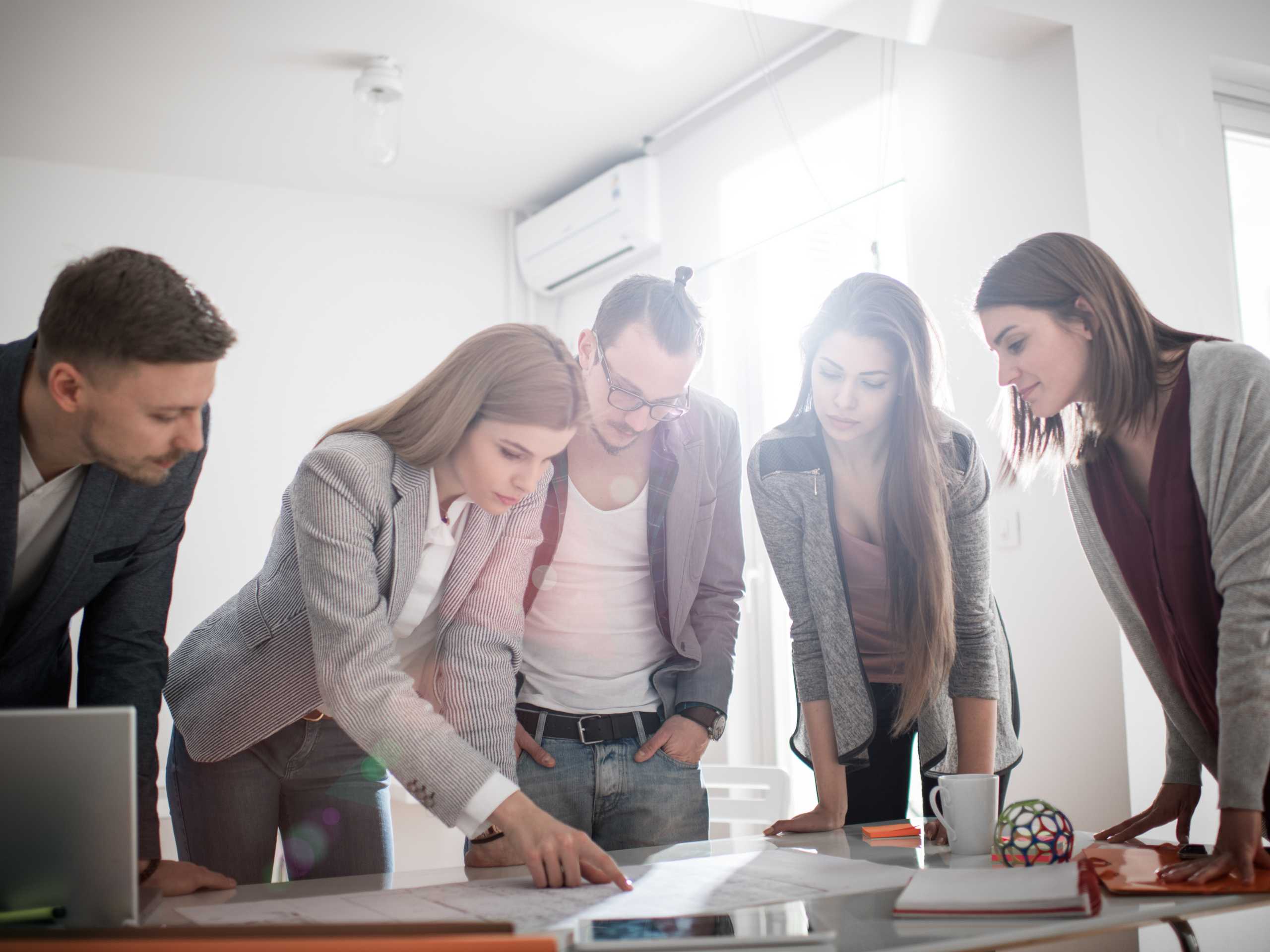 Gruppe von 5 Menschen, die über einen Tisch lehnen und etwas besprechen bzw zusammen Brainstormen.